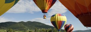 Multiple multicolored hot air balloons take off from a field in Napa with rolling green hills in the background.