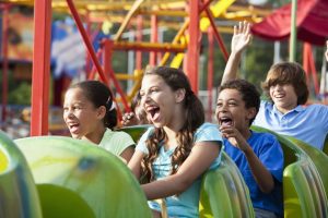 Four preteens laugh and shriek as they ride a small roller coaster at a local fair.