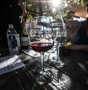 A red wine glass sits on a rustic picnic table in Napa with the sun shining behind it.