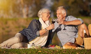 couple sitting on grass toasting with red wine