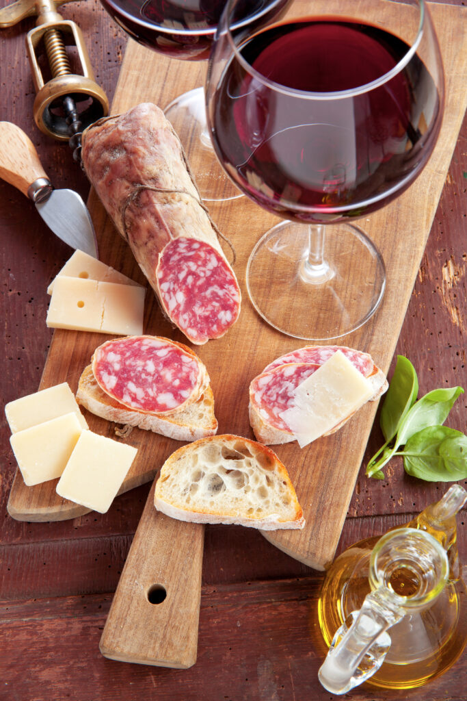 two wine glasses with red wine and assortment of cheese and salami and olive oil 