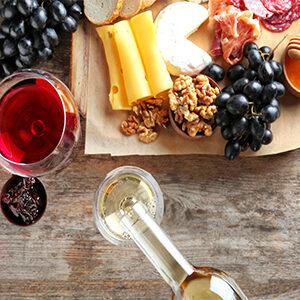 pouring white wine in glass on table with cheese and fruit board top view