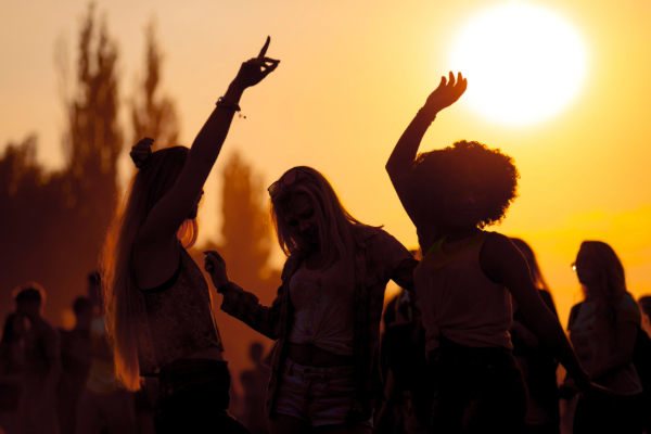group of friends dancing at summer festival at sunset